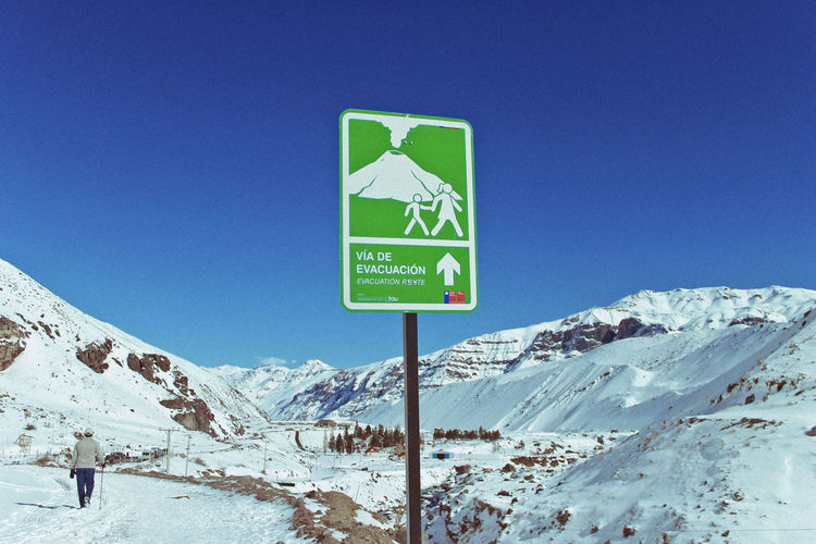 Road sign by snowcapped mountains against clear blue sky