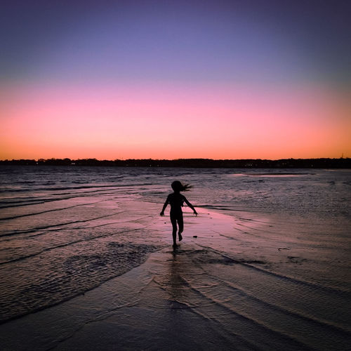Silhouette of girl walking at beach against sky during sunset