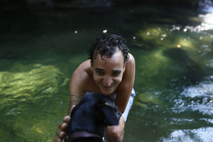 Portrait of happy man touching dog while enjoying in lake