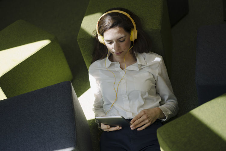 Woman with headphones using digital tablet while relaxing on floor in office