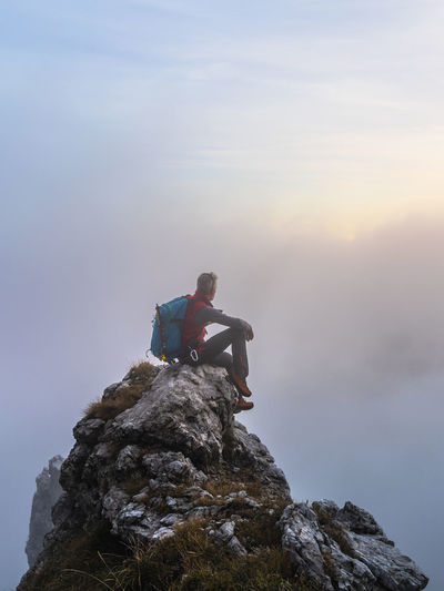 Pensive hiker sitting on mountain peak during sunrise at bergamasque alps, italy