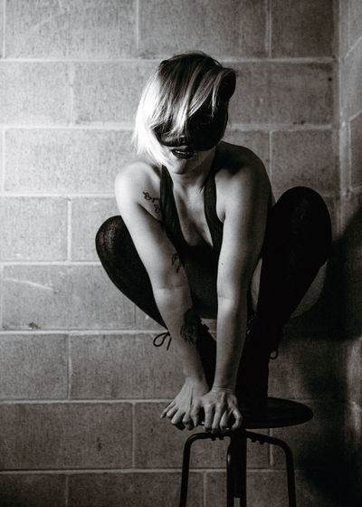 Portrait of woman wearing eye mask crouching on table against wall