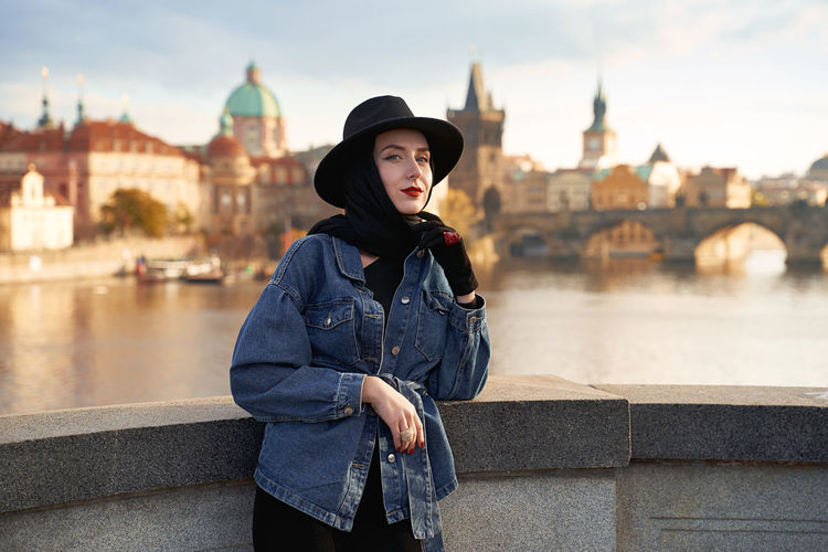 Stylish beautiful young woman earing black hat in prague with charles bridge on background. 