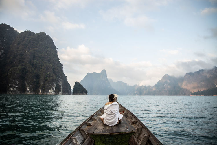 An asian woman in a white shirt sits in front of a boat trip in thailand. amazing thailand.