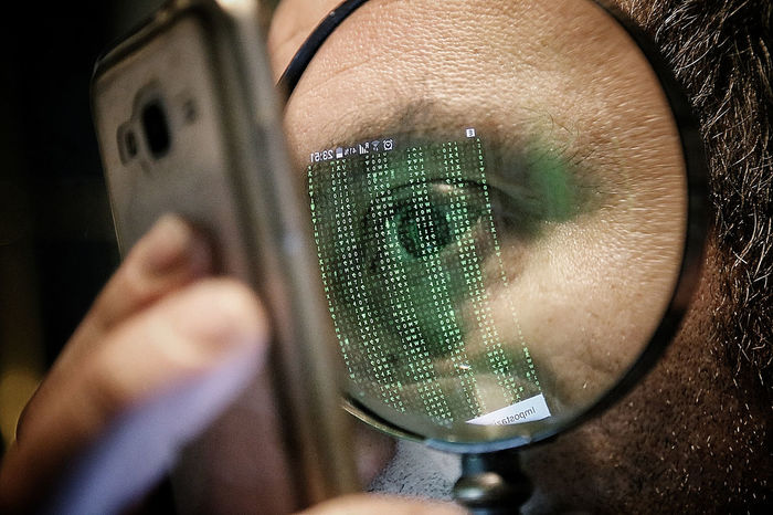 Cropped image of man looking at mobile phone through magnifying glass
