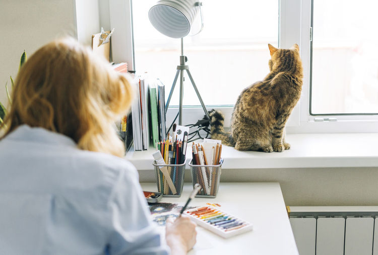Rear view of woman with cat sitting on table