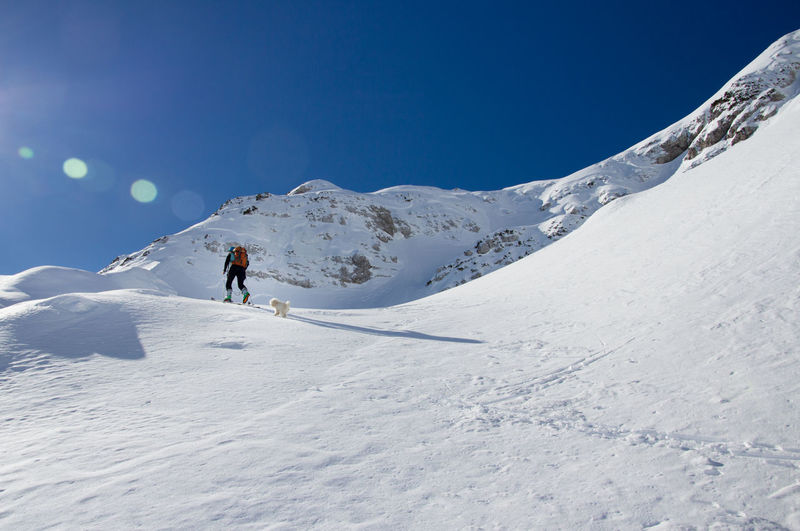 Woman with dog walking on snowcapped mountain against sky