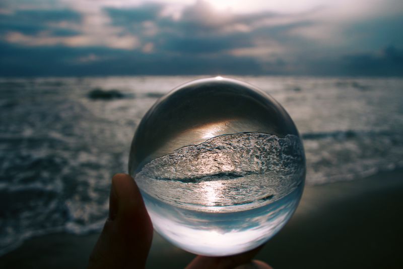 Close-up of hand holding crystal ball against sea