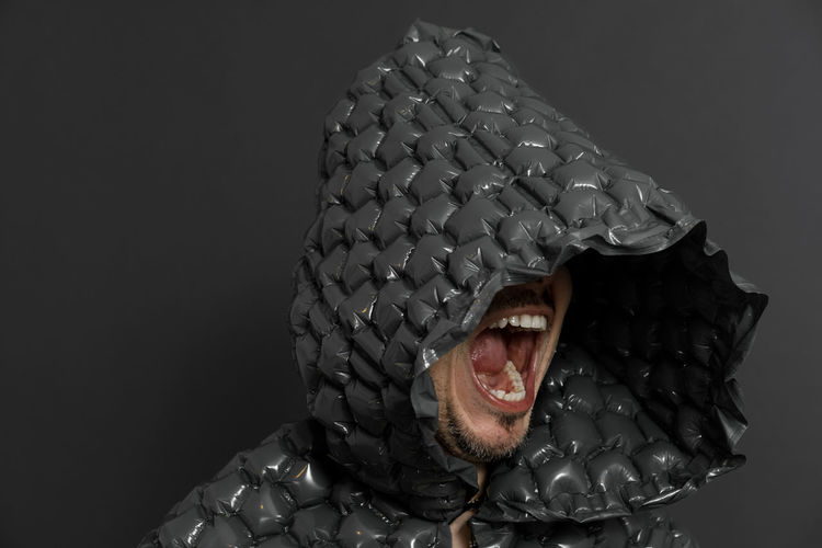 Close-up of man screaming while wearing hood against black background