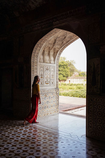 Full body asian woman walking through ornamental arch while leaving dark tomb of itimad-ud-daulah in agra, india