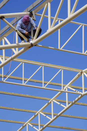 Low angle view of child on metallic structure against blue sky