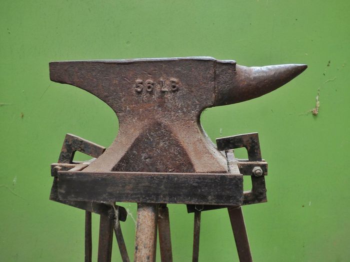 Close-up of old anvil against green wall