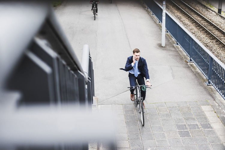 Young businessman riding bike while talking on the phone