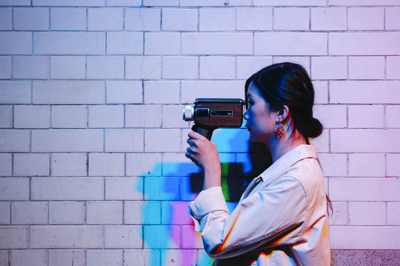 Young woman photographing against wall