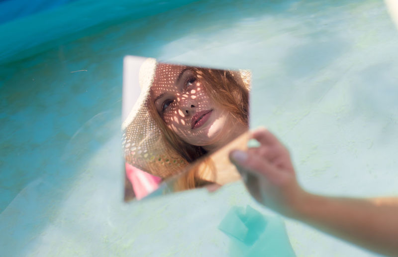 Young woman holding mirror with reflection in wading pool