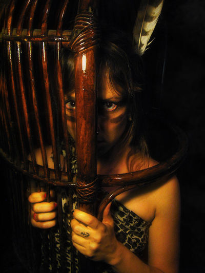 Portrait of girl in tribe costume looking through wooden shield at night
