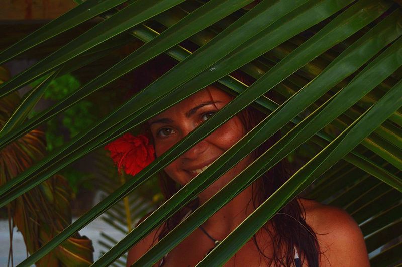 Close-up portrait of smiling woman by palm leaves