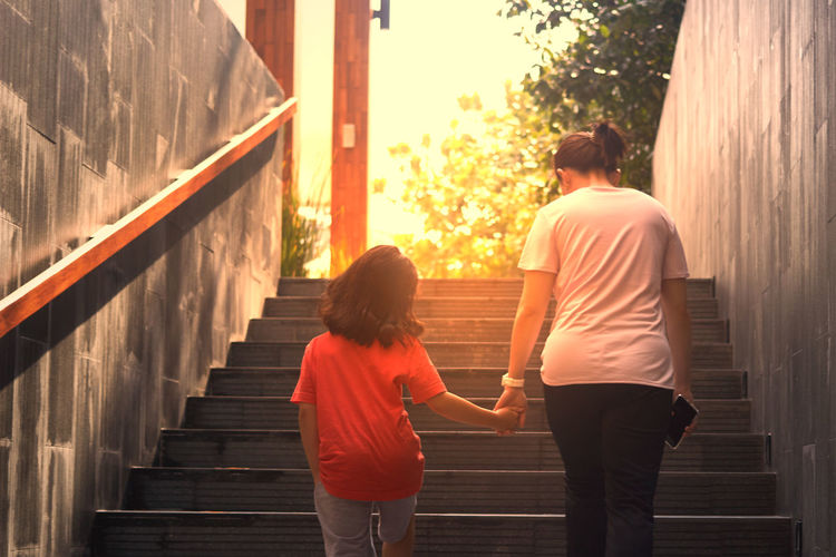 Rear view of mom and daughter walking on staircase togetherness 