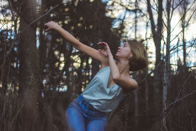 Young woman dancing against trees in forest