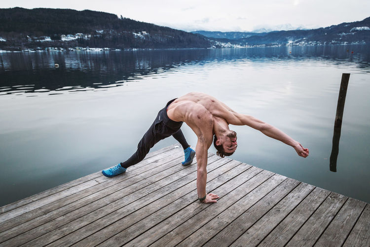Full length of shirtless man standing on pier over lake