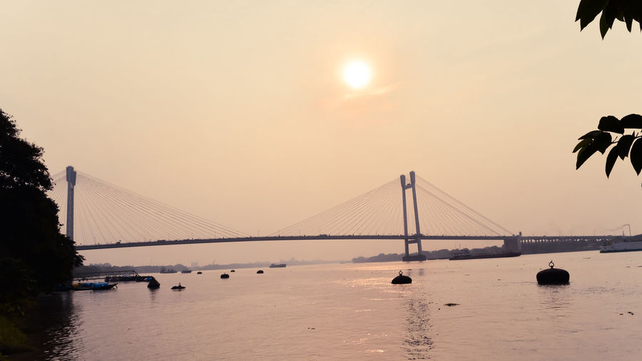 Hooghly bridge over river against sky during sunset