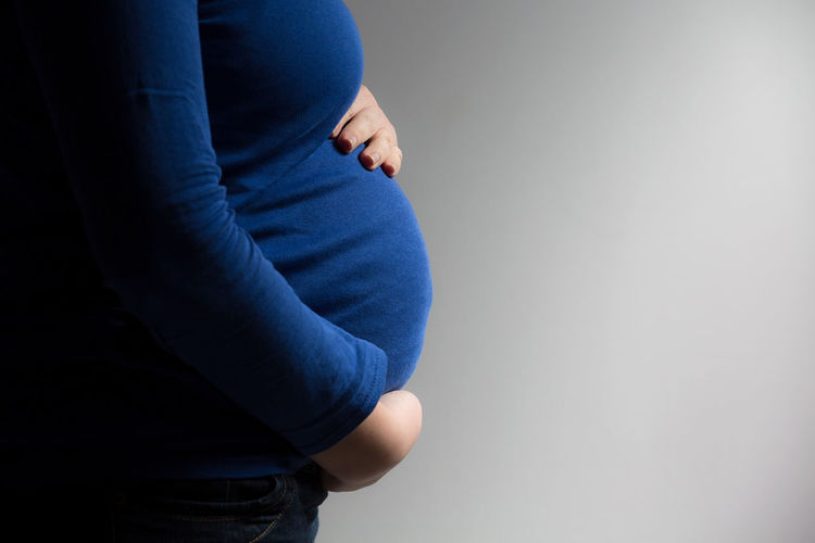 Midsection of pregnant woman standing against gray background