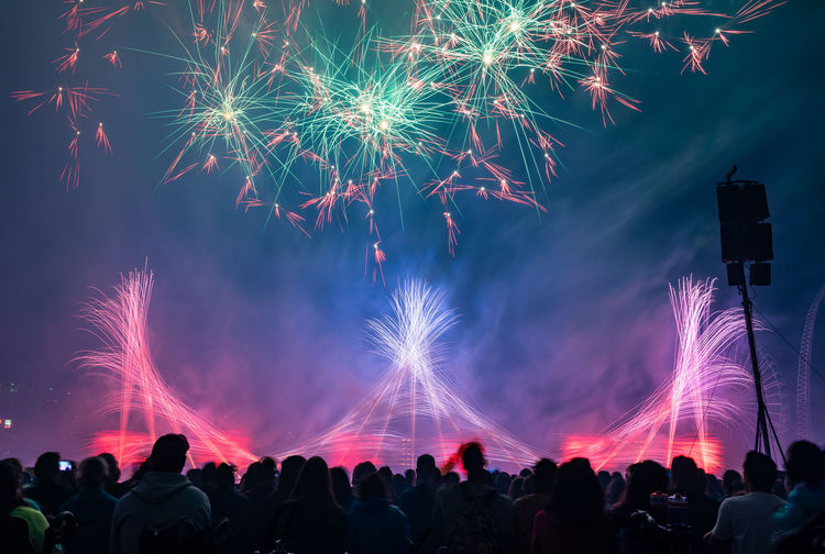 Crowd against firework display in sky at night