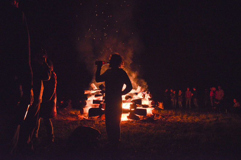 Silhouette people enjoying by bonfire on field against sky at night