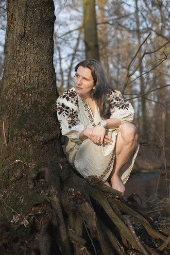 Close up woman in linen dress with embroidery sitting near tree portrait picture