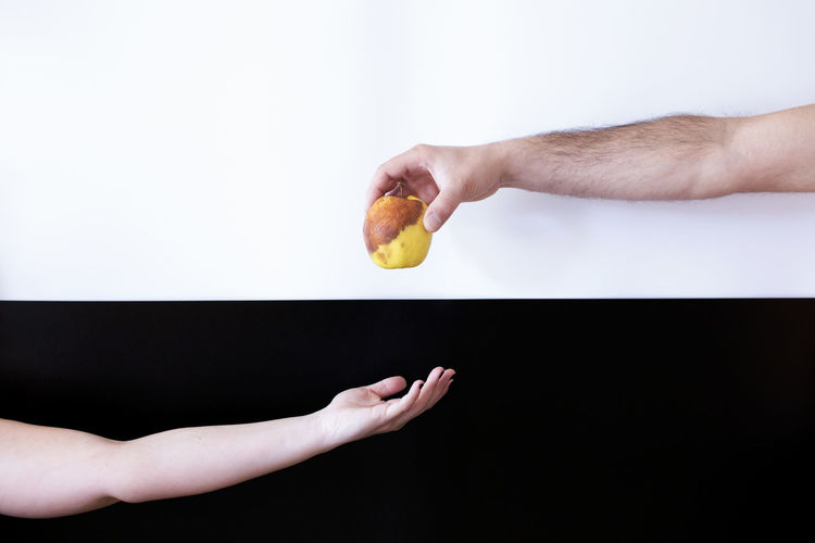Cropped hand giving rotten apple to person against two tone background