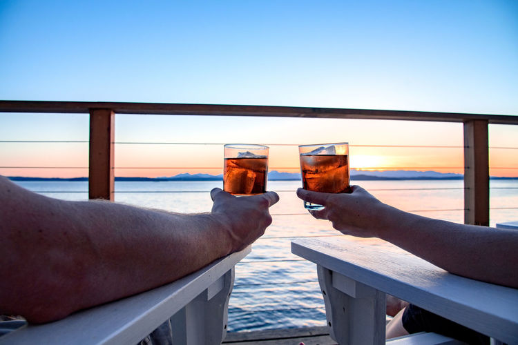 Cropped image of couple drinking whiskey on pier against sky