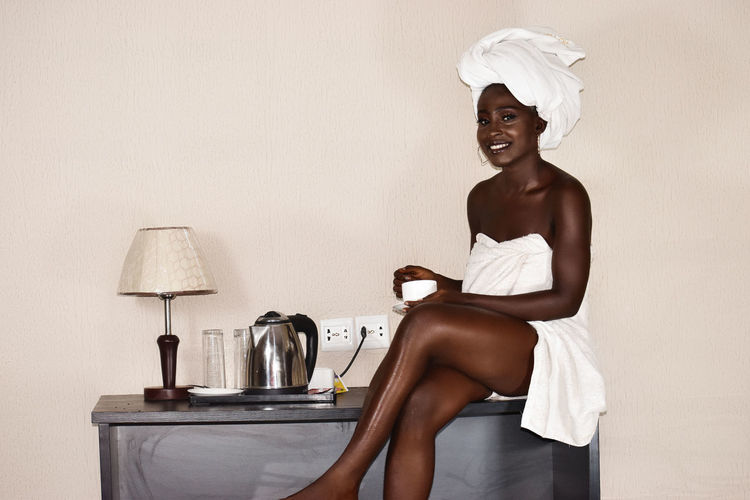 Portrait of woman wearing towel sitting by wall