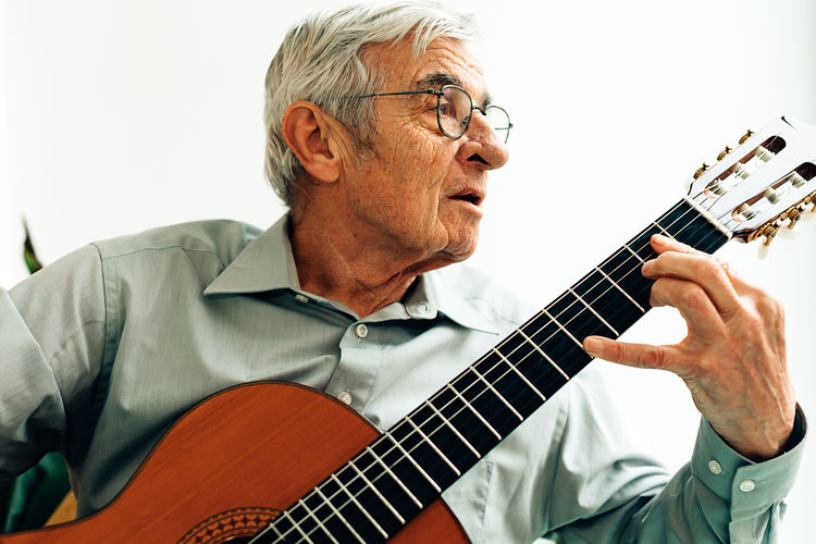 Elderly man playing on acoustic guitar at home. senior person with music hobby.
