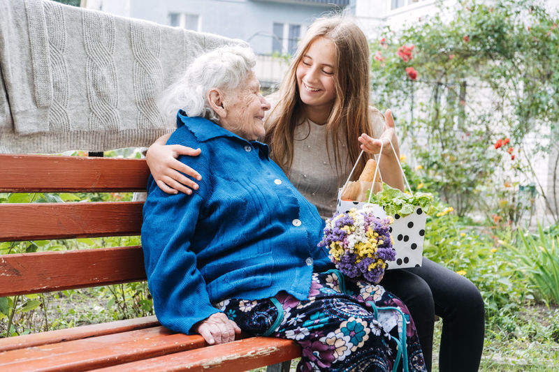 Volunteer girl and senior elderly woman with gift, flowers bouquet and basket of groceries