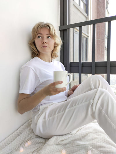 Young woman drinking coffee cup on bed at home