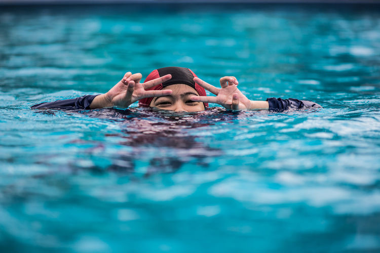 Portrait of woman making peace sign while swimming in pool