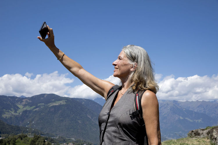 Smiling senior woman taking selfie through smart phone on sunny day