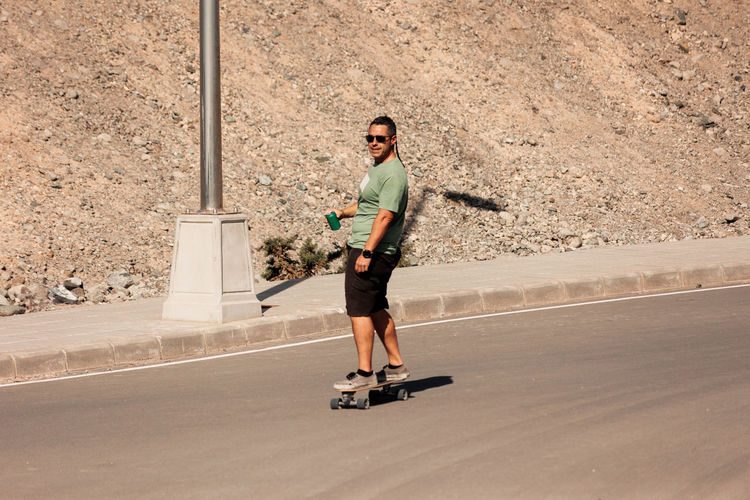 A man playing figure skating on a rural road in the sun on a bright day, play surf skate