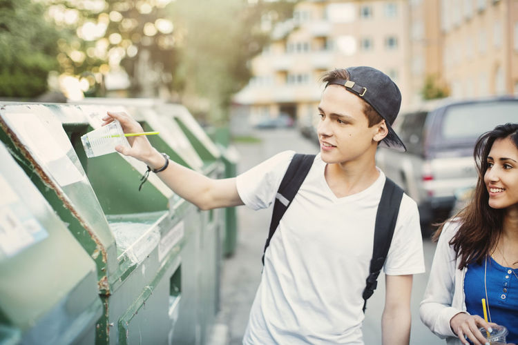 Teenager putting disposable glass in garbage bin on street