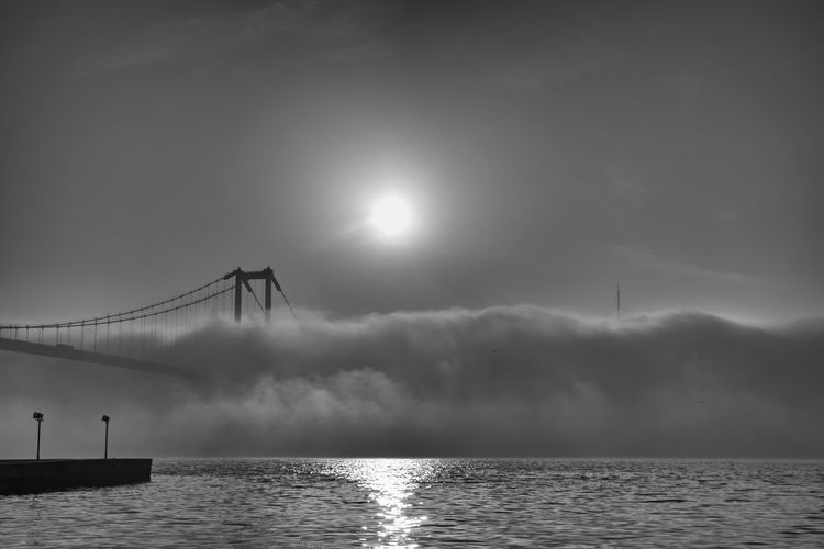 Silhouette bridge over sea against sky and fog