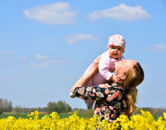 Portrait of happy girl with arms raised on field against sky