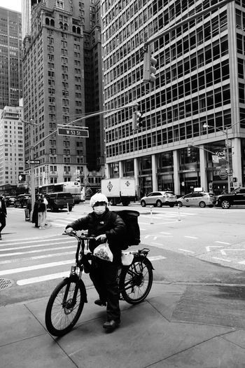 Man riding bicycle on city street against modern buildings