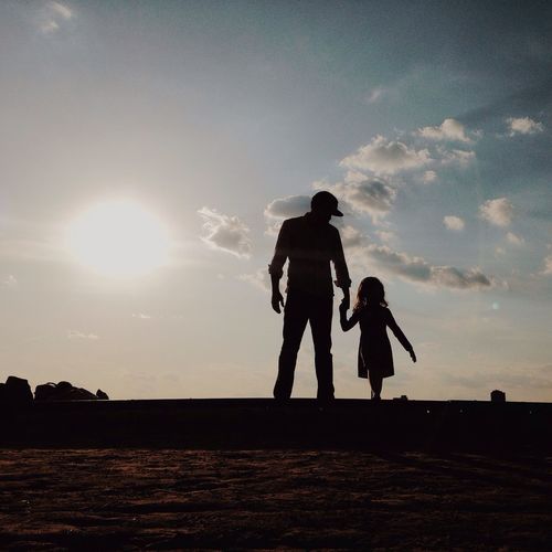Silhouette father with daughter standing on field against sky