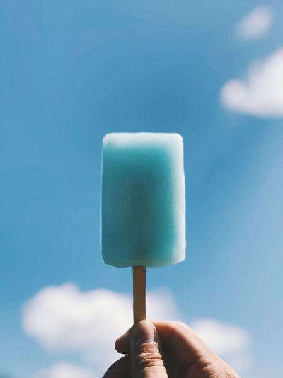 Close-up of hand holding flavored ice against blue sky