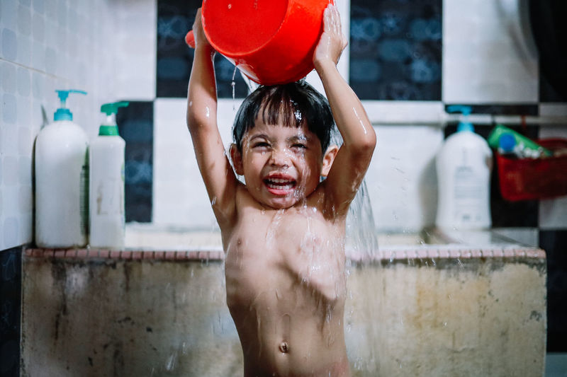 Portrait of shirtless boy happily taking a shower at the village