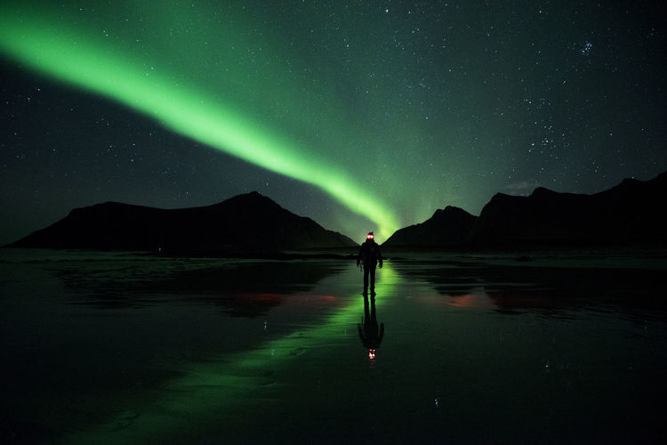 Mans standing on frozen lake while standing against aurora