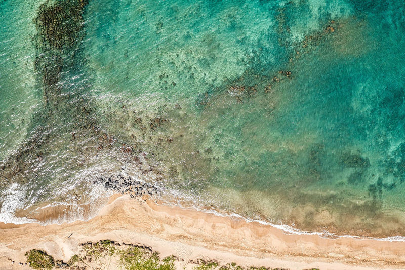 Top down view into teal water from beautiful hawaiian island of maui with white sand beach