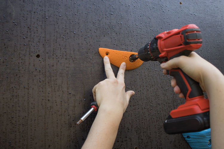 Unrecognizable mechanic using electric screwdriver and fixing grips on climbing wall in gym