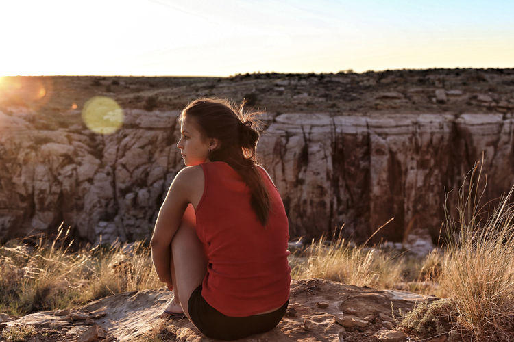 Rear view of young woman sitting on mountain against clear sky during sunset