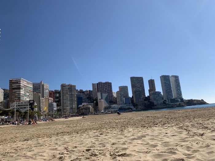 Panoramic view of beach and buildings against clear blue sky